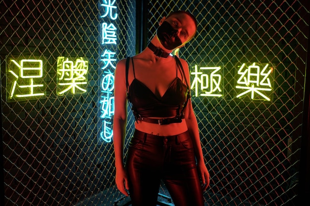 Donna cyberpunk in piedi in costume di pelle con la faccia dipinta contro le sbarre con geroglifici al neon che significano nirvana e paradiso occidentale