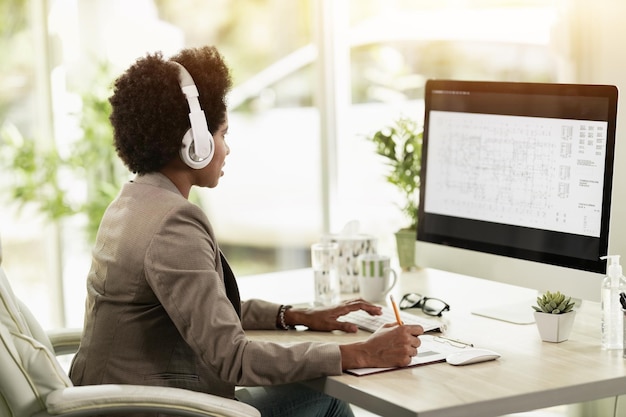 Donna d'affari afroamericana con le cuffie che controlla il progetto e pianifica su Internet mentre si siede al computer in un ufficio da solo al lavoro.