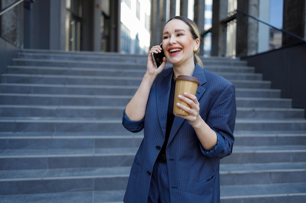 Donna d'affari allegra con una tazza di caffè in mano a parlare al telefono