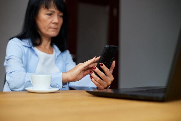 Donna d'affari anziana che si rilassa sul posto di lavoro utilizzando il telefono cellulare