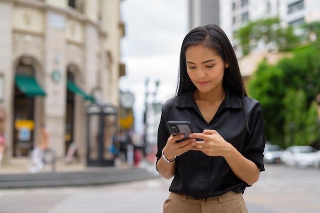 Donna d'affari asiatica all'aperto in una strada cittadina utilizzando il telefono cellulare mentre manda un sms