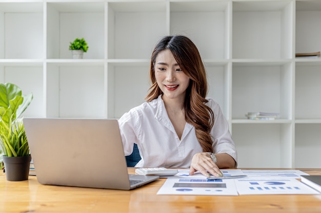 Donna d'affari asiatica che digita laptop nel suo ufficio privato, sta usando il suo laptop per digitare, inviare messaggi di lavoro con un partner, usa internet messenger. Concetto asiatico della donna di affari.