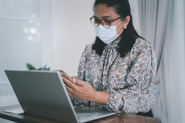 Donna d'affari asiatica che indossa una maschera per proteggere il coronavirus per lavorare da casa