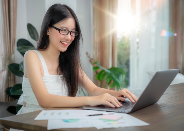 Donna d'affari asiatica che lavora in ufficio a casa sul tavolo con un notebook per computer e una tazza di caffè