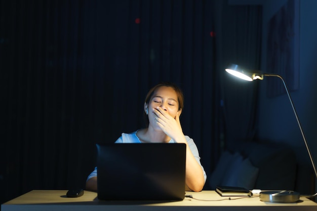 Donna d'affari asiatica che lavorava sul suo laptop per prepararsi per la presentazione di domani mattina di notte sembrava così assonnata e stanca che sbadigliava a tarda notte nel soggiorno di casa