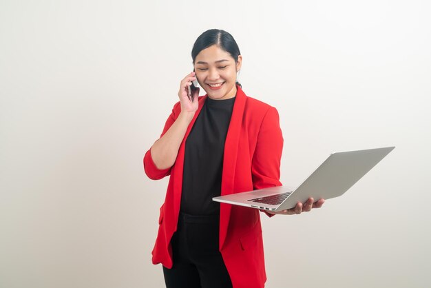 Donna d'affari asiatica che parla al telefono con la mano che tiene il computer portatile su sfondo bianco