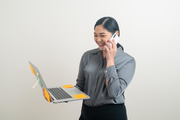 Donna d'affari asiatica che parla al telefono con la mano che tiene il computer portatile su sfondo bianco