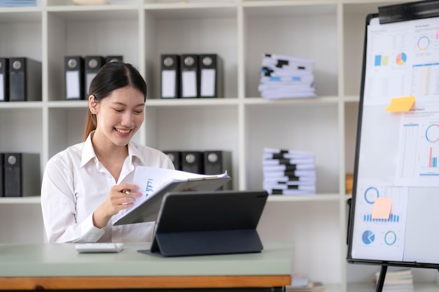 Donna d'affari asiatica che si concentra sulle scartoffie e prepara i rapporti, analizza il lavoro Fare scartoffie al lavoro utilizzando il software per computer online in ufficio