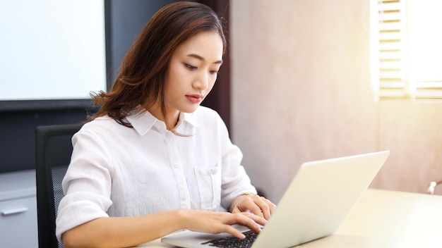 Donna d'affari asiatica che utilizza il laptop per lavoro e fa ricerche su Internet nel suo ufficio