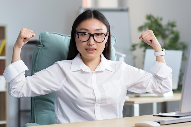 Donna d'affari asiatica di successo guardando la telecamera e alzando le mani un gesto di super