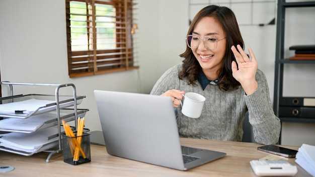 Donna d'affari asiatica professionista che agita la mano per salutare la sua squadra tramite una riunione online