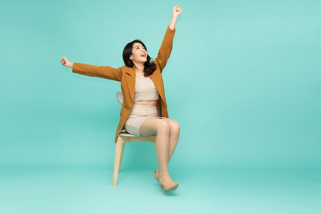 Donna d'affari asiatica seduta su una sedia e con le mani in alto le braccia alzate dalla felicità