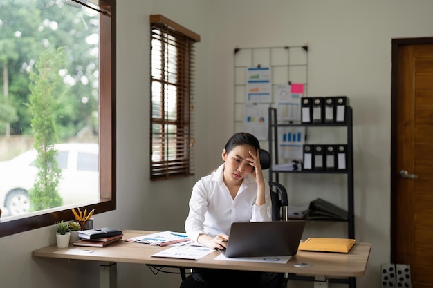 Donna d'affari asiatica stanca con mal di testa in ufficio che si sente male al lavoro