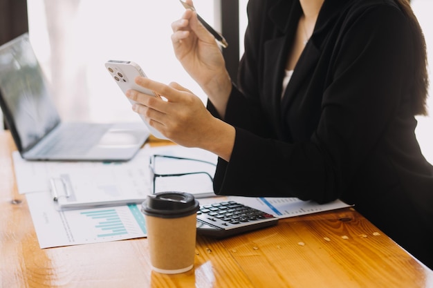 Donna d'affari asiatica Utilizzando il computer portatile e lavorando in ufficio con il documento della calcolatrice sulla scrivania facendo pianificazione analizzando il concetto di analisi finanziaria di investimento del piano aziendale della relazione finanziaria