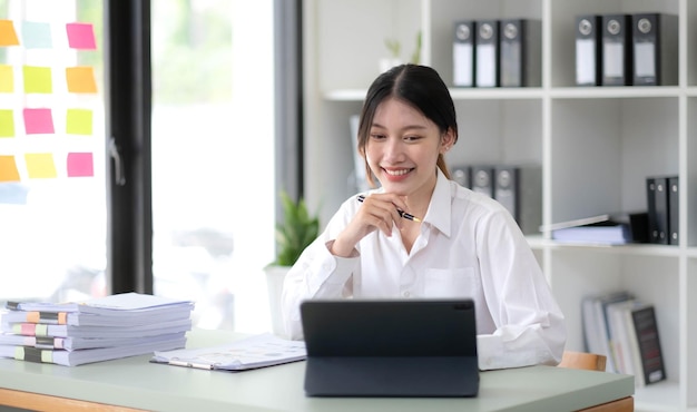 Donna d'affari asiatica Utilizzando il computer portatile e lavorando in ufficio con il documento della calcolatrice sulla scrivania facendo pianificazione analizzando il concetto di analisi finanziaria di investimento del piano aziendale della relazione finanziaria