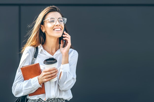 Donna d'affari che cammina e parla al cellulare all'aperto vicino al moderno centro business con il taccuino.