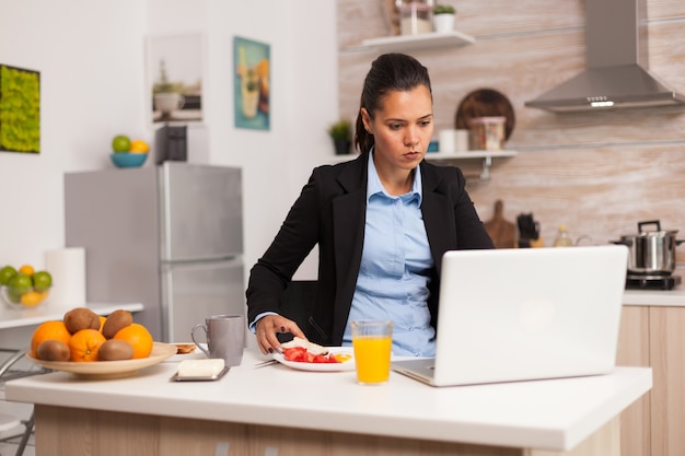 Donna d'affari che fa colazione e lavora al computer portatile