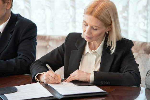 Donna d'affari che firma la carta mentre è seduta accanto al delegato straniero