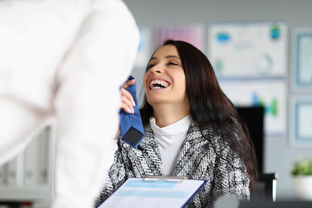 Donna d'affari che flirta con un lavoratore maschio aziendale che si tocca la cravatta e ride