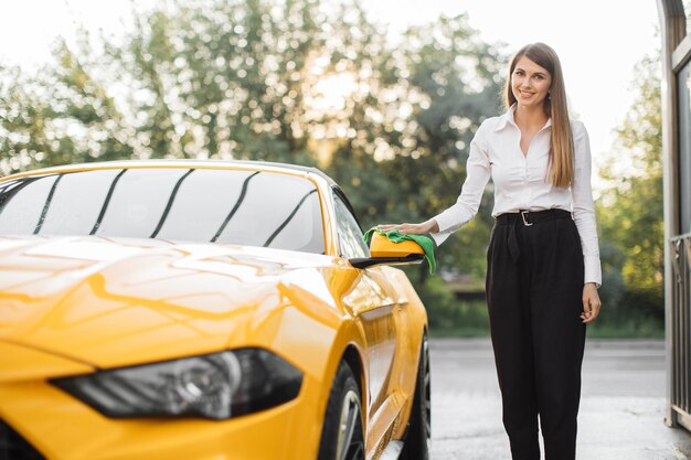 Donna d'affari che indossa una camicia bianca e pantaloni neri che puliscono lo specchietto retrovisore dell'auto