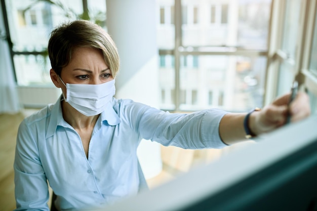 Donna d'affari che indossa una maschera facciale mentre lavora su un PC desktop in ufficio