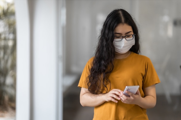 donna d'affari che indossa una maschera protettiva casual e scrive un messaggio sullo smartphone che lavora con il laptop