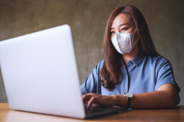 Donna d'affari che indossa una maschera protettiva mentre lavora su un computer portatile in ufficio