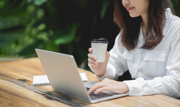 Donna d'affari che lavora su un laptop e tiene una tazza di caffè caldo su un tavolo di legno con una tazza di caffè Il concetto di business lavora a casa ovunque