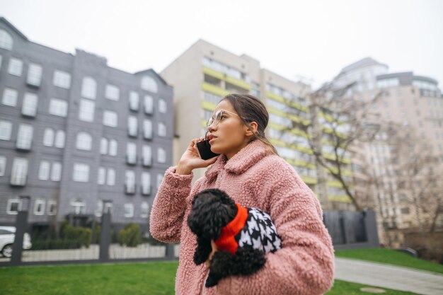 Donna d'affari che parla al telefono e porta a spasso il cane che tiene nelle sue mani