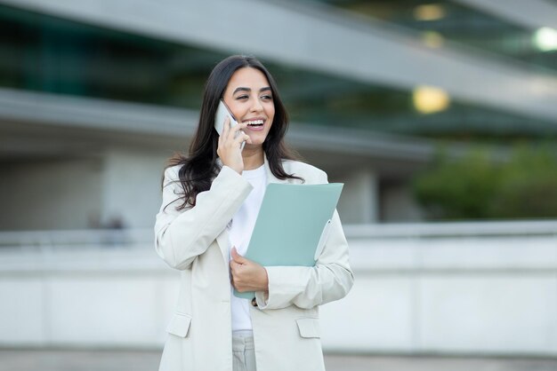 Donna d'affari che parla al telefono e tiene documenti fuori dall'edificio degli uffici