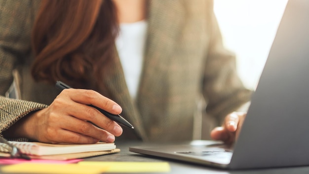 Donna d'affari che scrive su documenti durante la digitazione sul computer portatile sul tavolo in ufficio