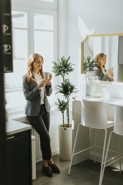 Donna d'affari che si gode una pausa caffè mattutina in una cucina moderna illuminata dal sole