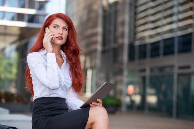 Donna d'affari che usa il suo telefono cellulare mentre tiene in mano un tablet