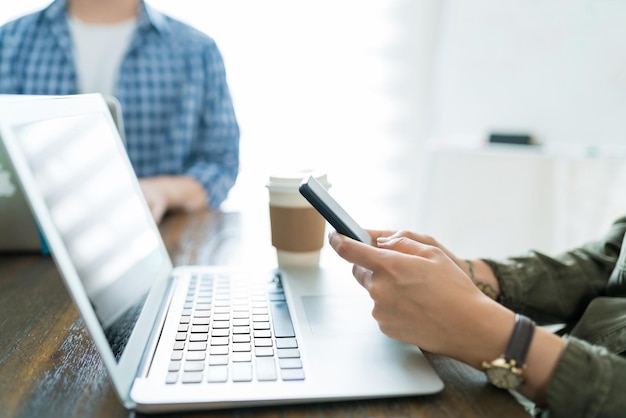 Donna d'affari che utilizza il laptop durante la messaggistica sullo smartphone alla scrivania in ufficio