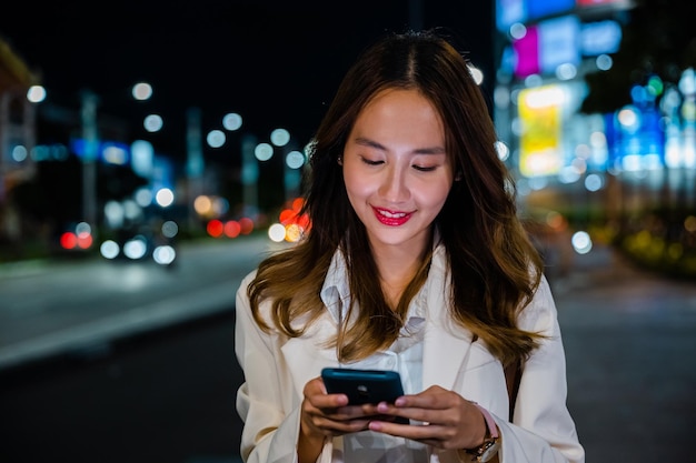 Donna d'affari che utilizza il telefono cellulare camminando per la strada della città di notte