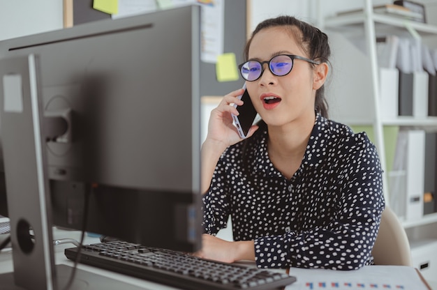 Donna d'affari con gli occhiali che parla al telefono con il cliente sul posto di lavoro Donna d'affari