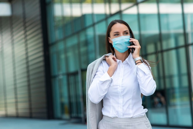 Donna d'affari con maschera che parla al telefono all'aperto