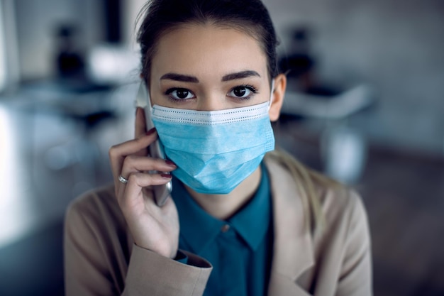 Donna d'affari con maschera protettiva che parla al cellulare in ufficio