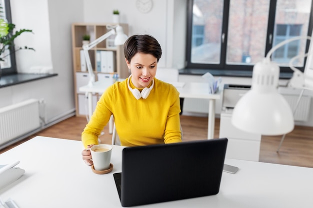 donna d'affari con un laptop che beve caffè in ufficio