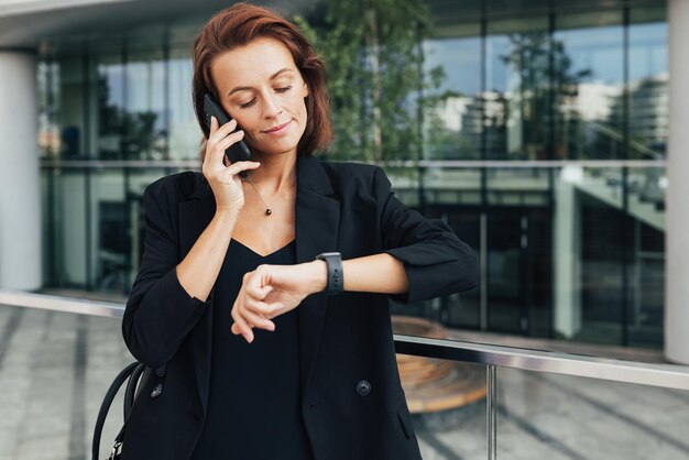 Donna d'affari di mezza età che guarda il suo smartwatch mentre parla al cellulare