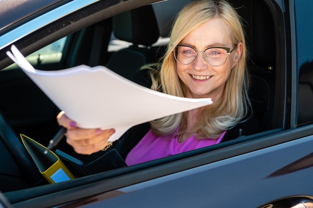 Donna d'affari di mezza età con gli occhiali che dà documenti attraverso il finestrino dell'auto si concentra sul viso