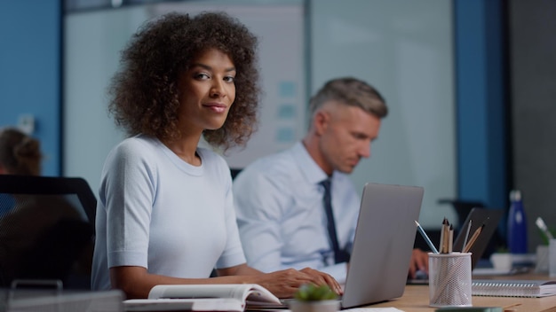 Donna d'affari di razza mista che utilizza computer portatile Dirigente femminile che gira la testa alla telecamera