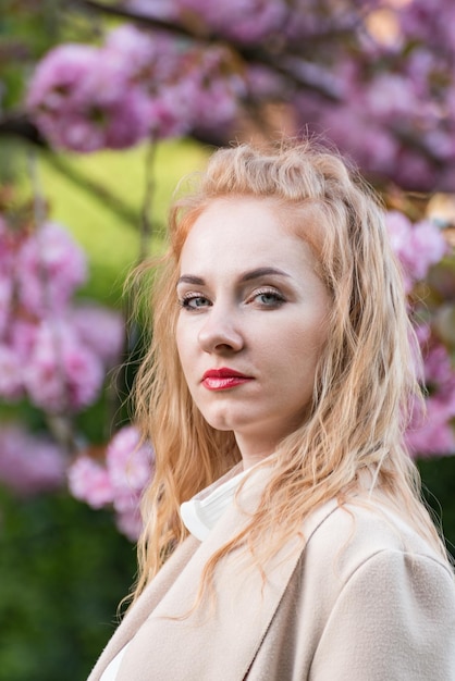 Donna d'affari di successo all'aperto Ritratto di donna bionda con labbra rosse vicino albero in fiore Telaio verticale