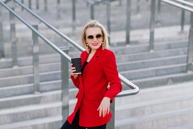 Donna d'affari di successo in cappotto rosso parlando su smartphone negoziando un affare sullo sfondo di alti edifici nel centro business.