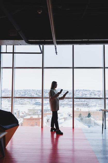 Donna d'affari di successo in piedi a guardare fuori dalla finestra godendosi la vista della città donna ricca e sicura di sé che pensa al successo aziendale e alla visione per il futuro pianificando nuovi obiettivi