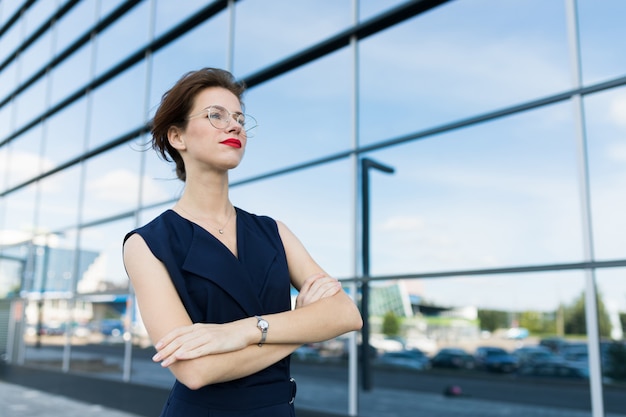 Donna d'affari di successo in posa sullo sfondo di un edificio a specchio con la riflessione di nuvole e cielo