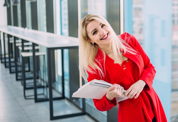 donna d'affari di successo in un abito rosso in un edificio per uffici leggero vicino alla finestra