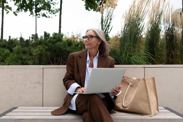 donna d'affari di un anno seduta con un computer portatile su una panchina sulla strada