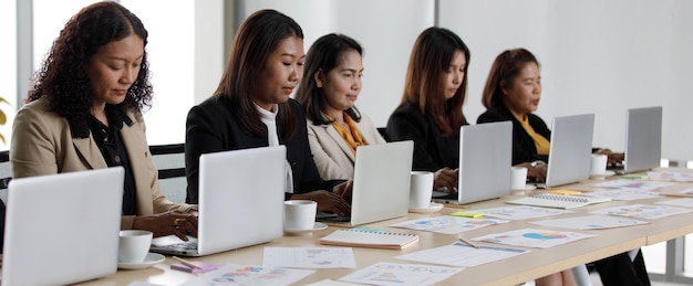 Donna d'affari femminile asiatica di mezza età non identificata irriconoscibile in abito formale seduto lavorando digitando computer portatile notebook insieme fianco a fianco sul tavolo pieno di documenti di relazione.