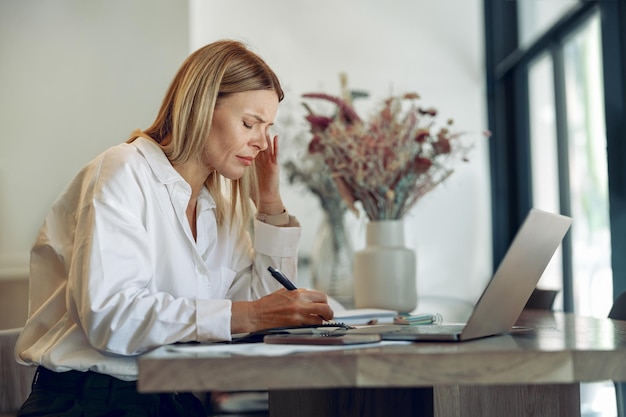 Donna d'affari focalizzata che lavora su un computer portatile che prende appunti nell'accogliente spazio interno del coworkign